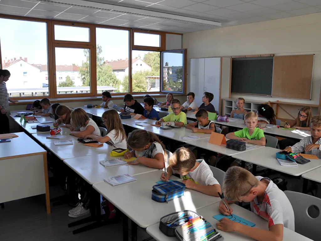 Kinder packen an ihren Plätzen Hefte und Mäppchen aus.